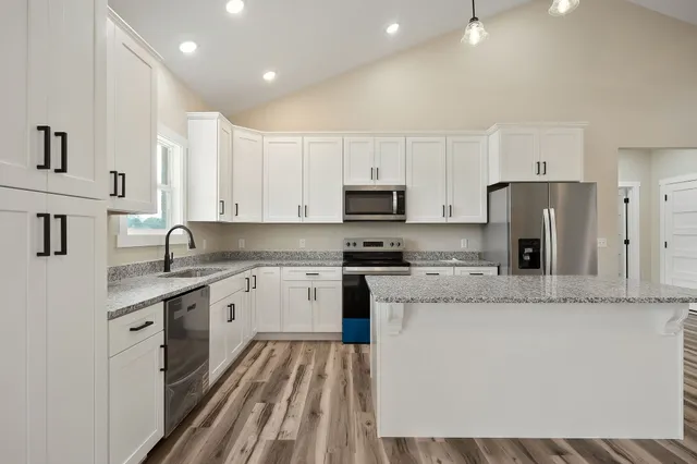 a large kitchen with stainless steel appliances granite countertop a stove a sink a refrigerator and white cabinets with wooden floor