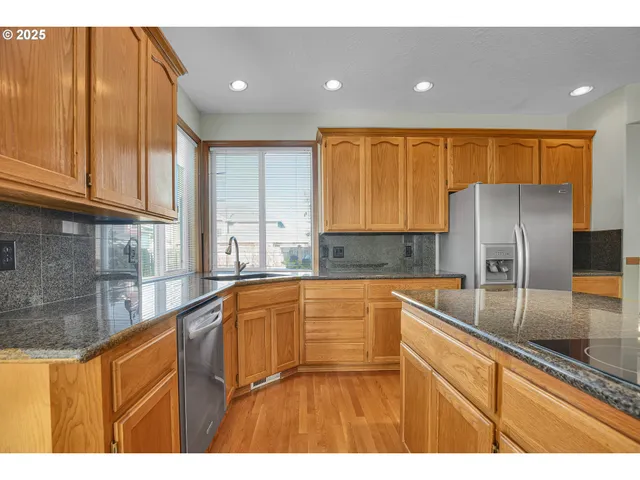 a kitchen with stainless steel appliances granite countertop a refrigerator a sink a stove with wooden cabinets