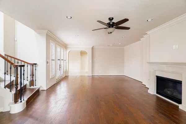 a view of an empty room with wooden floor a ceiling fan and windows