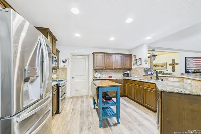 a kitchen with stainless steel appliances granite countertop a refrigerator a sink dishwasher a stove and white countertops with wooden floor