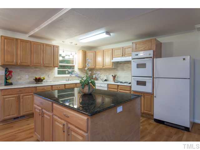 11709 Strickland Road Raleigh, NC 27613 - Photo 7 of 25 a kitchen with kitchen island a counter top space a sink a refrigerator and cabinets