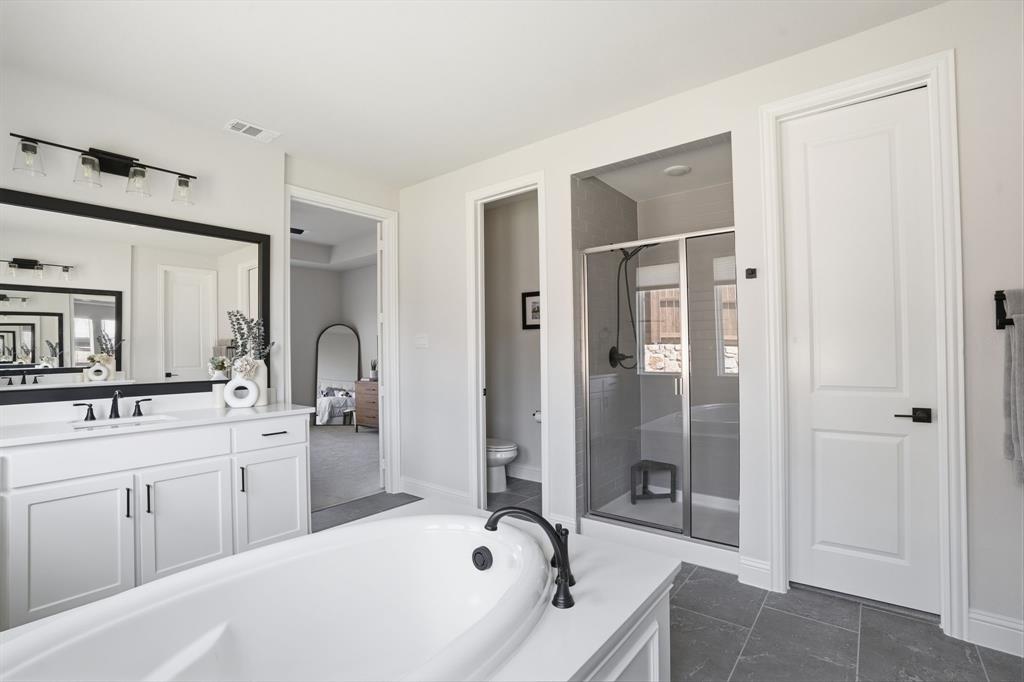 4202 Crown Run Road Midlothian, TX 76065 - Photo 15 of 34 Spacious bathroom featuring a freestanding soaking tub with black fixtures, a double vanity with white cabinetry and a large framed mirror, a glass-enclosed shower with tiled walls, and grey tile flooring