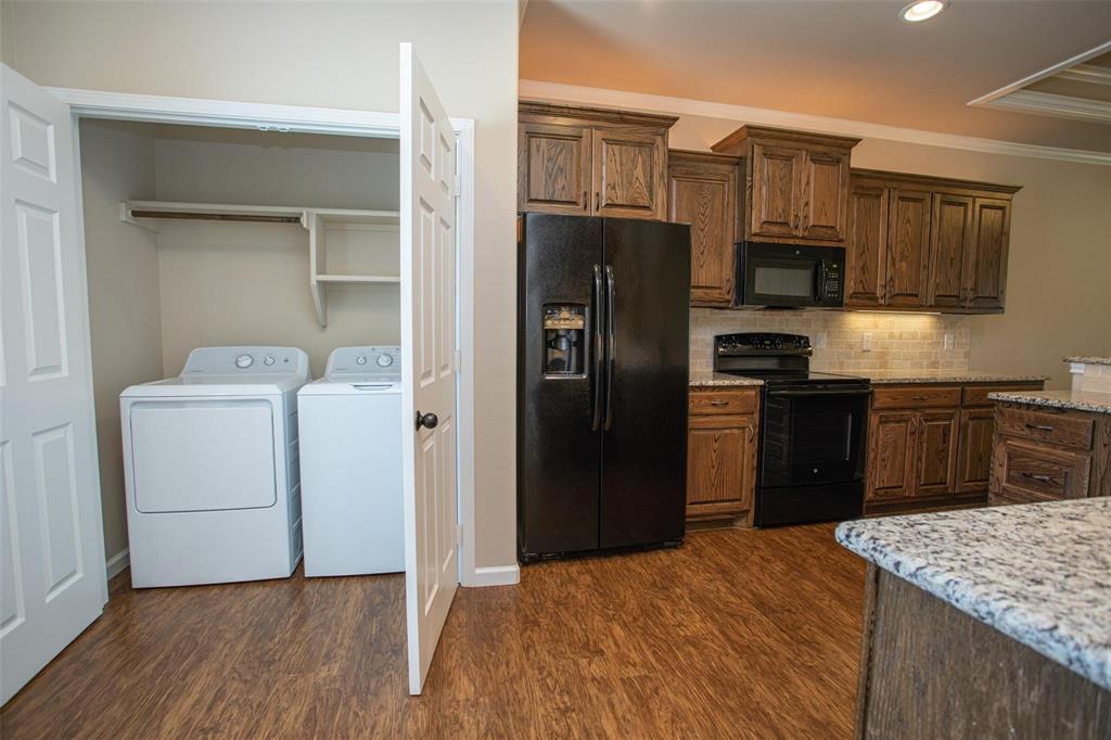 455 Neals Hill Road Oak Ridge, TX 76240 - Photo 10 of 19 Kitchen featuring black appliances, light stone counters, crown molding, tasteful backsplash, and dark wood finished floors