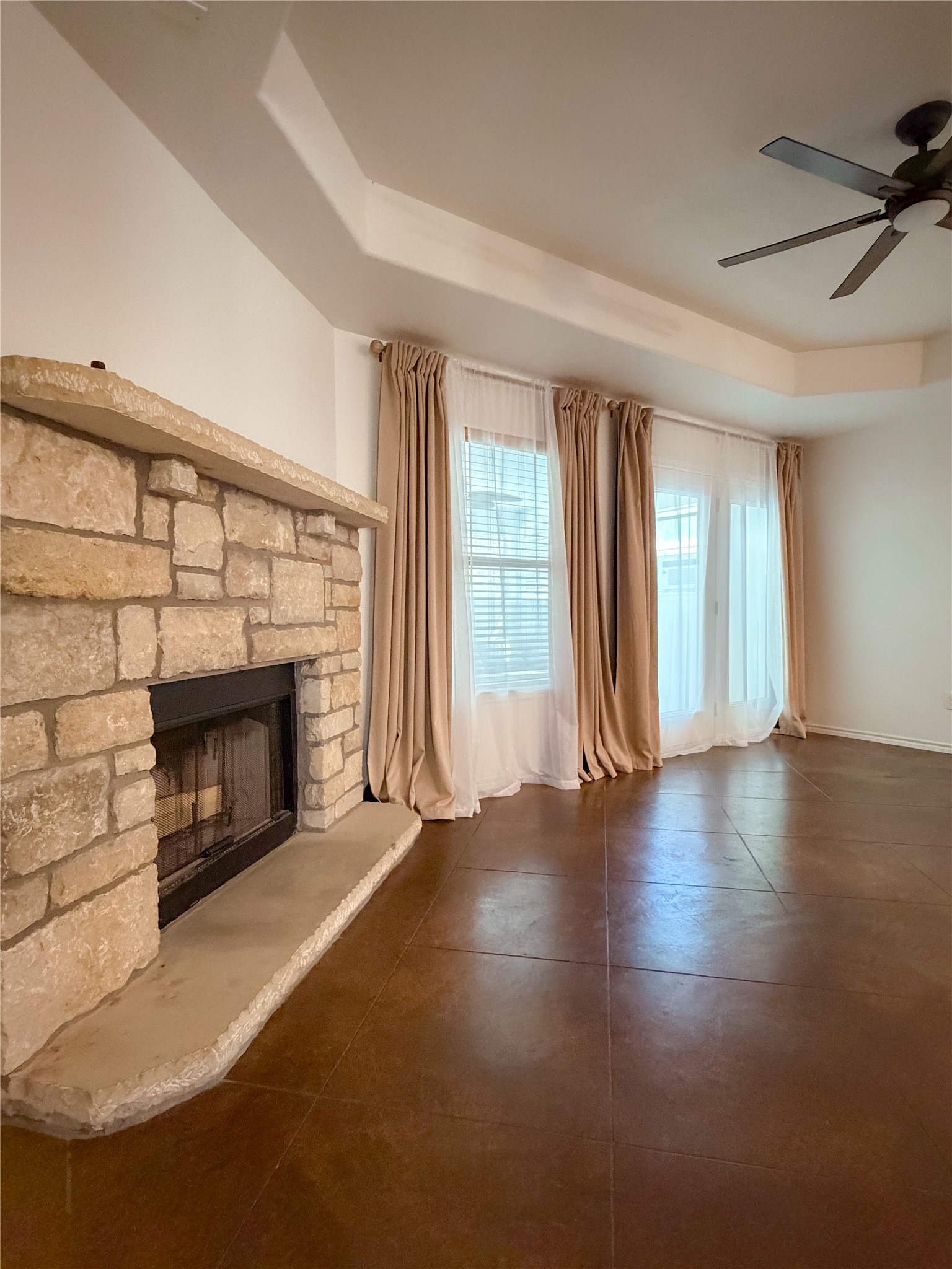 430 Summit Ridge Drive North Point Venture, TX 78645 - Photo 17 of 39 Unfurnished living room with a raised ceiling, a ceiling fan, a stone fireplace, and dark tile patterned floors
