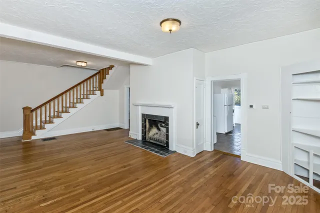 a view of an empty room with wooden floor and a fireplace