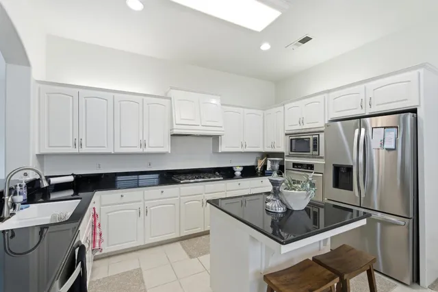a kitchen with kitchen island granite countertop a sink a stove white cabinets dining table and chairs