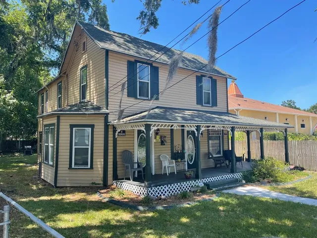 a view of a white house with a big yard potted plants and large tree
