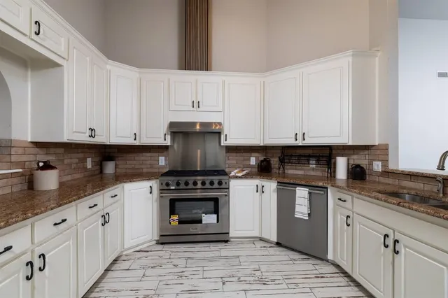 a kitchen with stainless steel appliances granite countertop a stove a sink and white cabinets