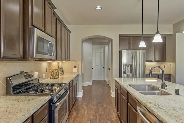 a kitchen with stainless steel appliances granite countertop a sink a stove and a wooden floors