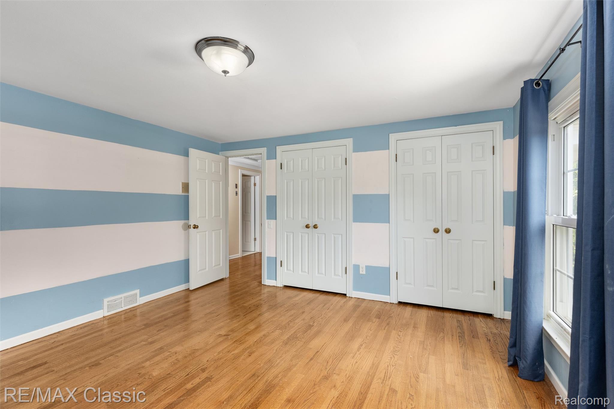 4268 Covered Bridge Road Bloomfield Hills, MI 48302 - Photo 19 of 35 Hardwood flooring throughout, featuring two bi-fold closet doors, a traditional semi-flush ceiling light fixture, and a window with a roller shade