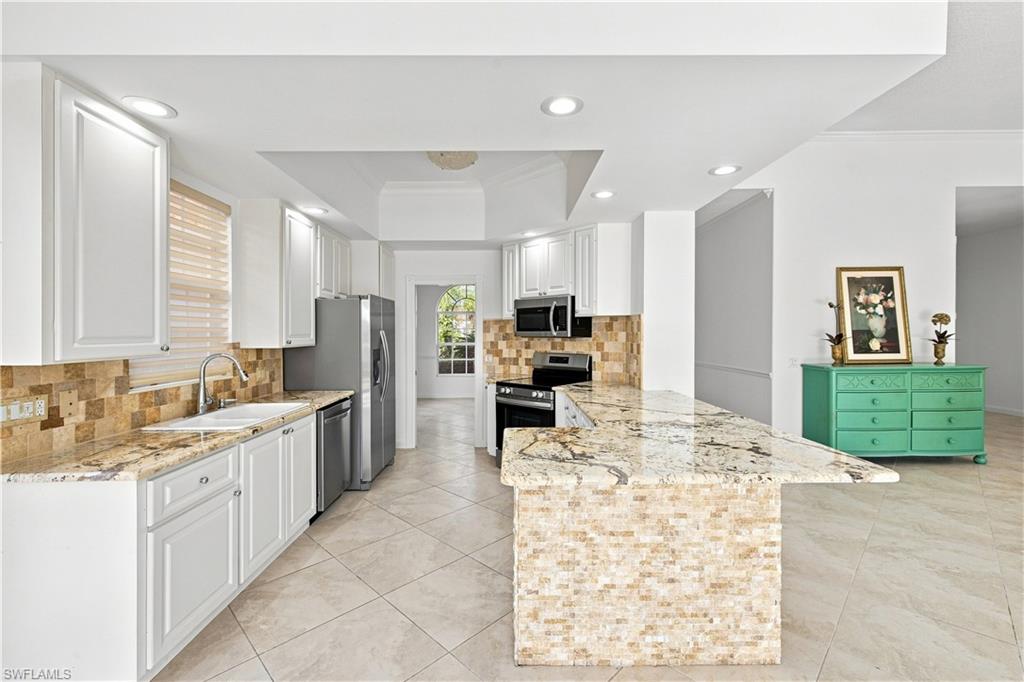 4470 Novato Court Naples, FL 34109 - Photo 4 of 33 Kitchen featuring white cabinetry, stone tile flooring, stainless steel appliances, a tile backsplash, and an island with a stone countertop