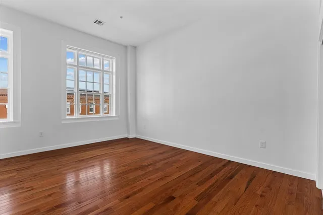 a view of an empty room with wooden floor and windows