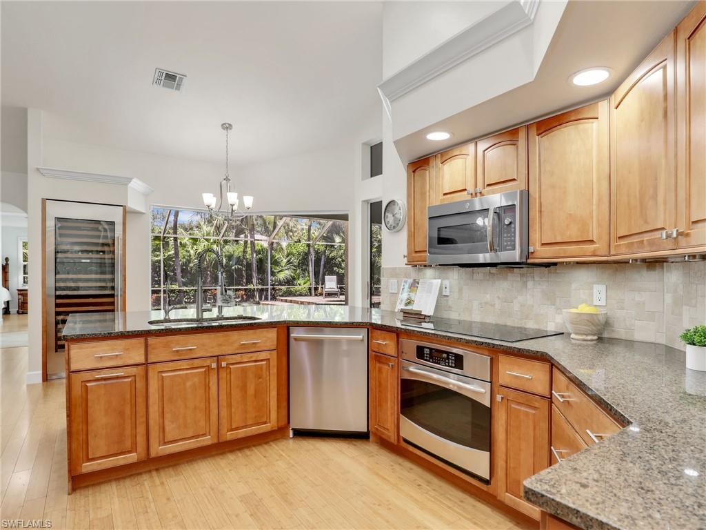 6862 Mill Run Road Naples, FL 34109 - Photo 12 of 50 Kitchen with decorative backsplash, light hardwood / wood-style flooring, stainless steel refrigerator with ice dispenser, and dark stone countertops