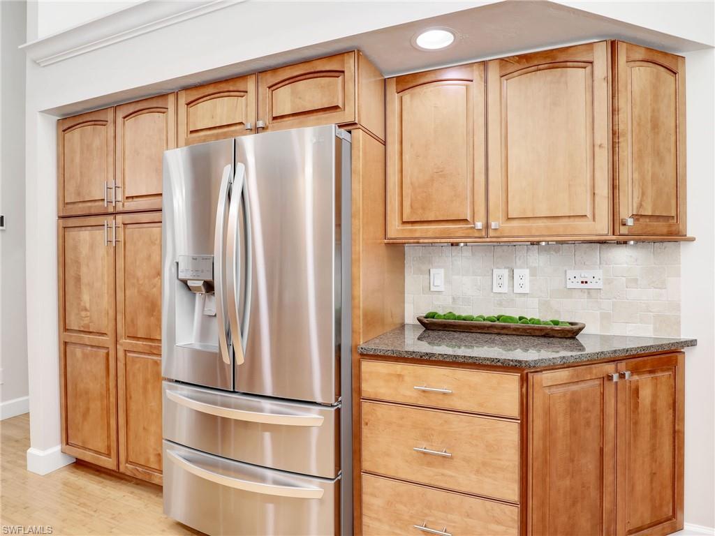 6862 Mill Run Road Naples, FL 34109 - Photo 13 of 50 Kitchen featuring appliances with stainless steel finishes, dark stone counters, light hardwood / wood-style flooring, decorative backsplash, and a high ceiling
