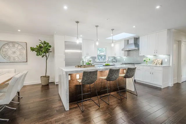 a room with stainless steel appliances kitchen island granite countertop a sink a counter space and wooden floor