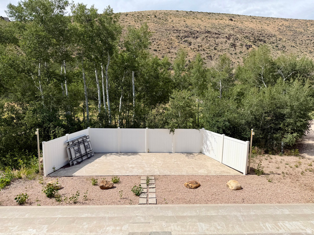 1133 Paris Canyon Road Paris, ID 83261 - Photo 45 of 75 Outdoor paved amphitheater area featuring a white privacy fence, gravel landscaping with decorative rocks, and mature trees in the background