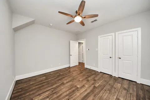 an empty room with wooden floor ceiling fan and windows