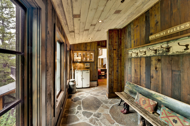 2983 East Ridgetop Road, Unit 27 Provo, UT 84604 - Photo 4 of 63 Rustic mudroom entry featuring reclaimed wood paneling throughout walls and ceiling, natural stone flooring with geometric patterning, large multi-pane windows with dark frames, vintage signage and architectural salvage displays, and direct access to adja
