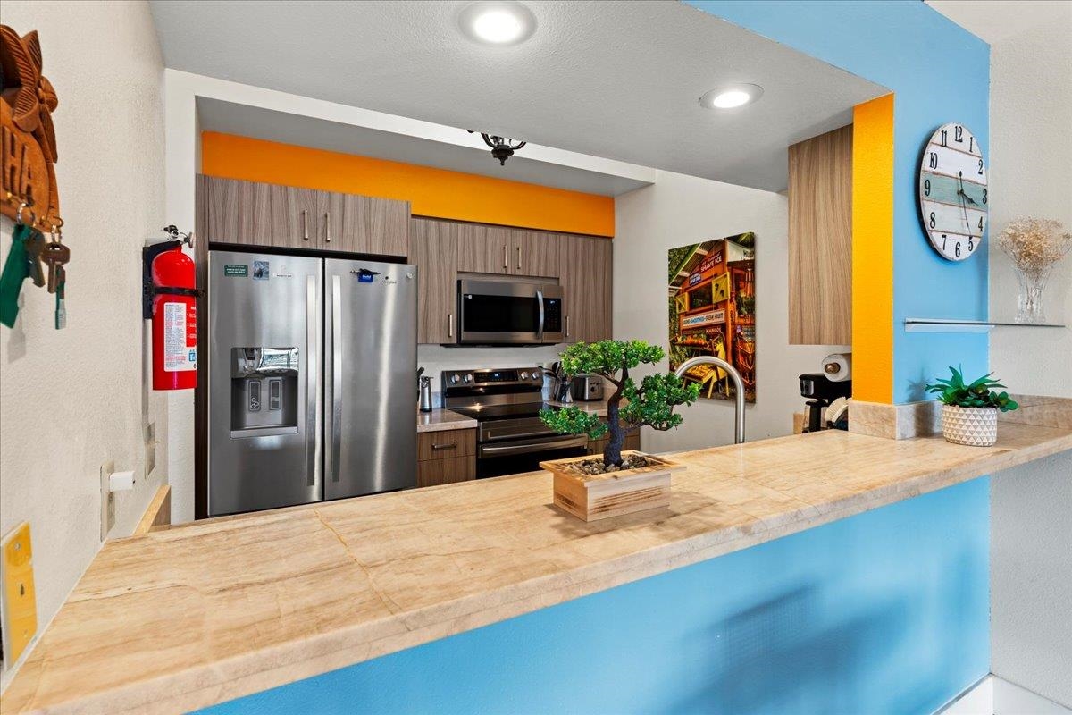 679 South Kihei Road, Unit D203 Kihei, HI 96753 - Photo 16 of 46 a kitchen with stainless steel appliances kitchen island granite countertop a refrigerator a stove and a sink with wooden floor