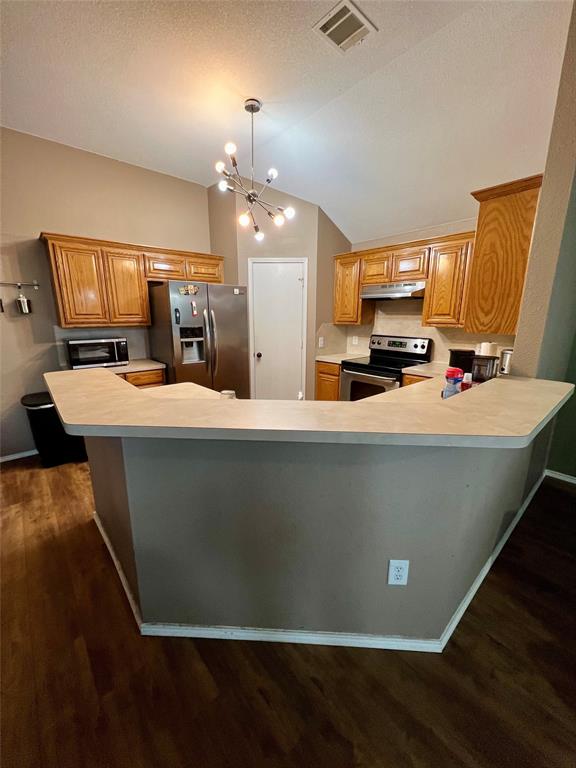 12201 Rolling Ridge Drive Fort Worth, TX 76028 - Photo 11 of 21 Kitchen featuring wood-finish cabinetry, stainless steel appliances, a breakfast bar with a neutral countertop, and wood-finish flooring