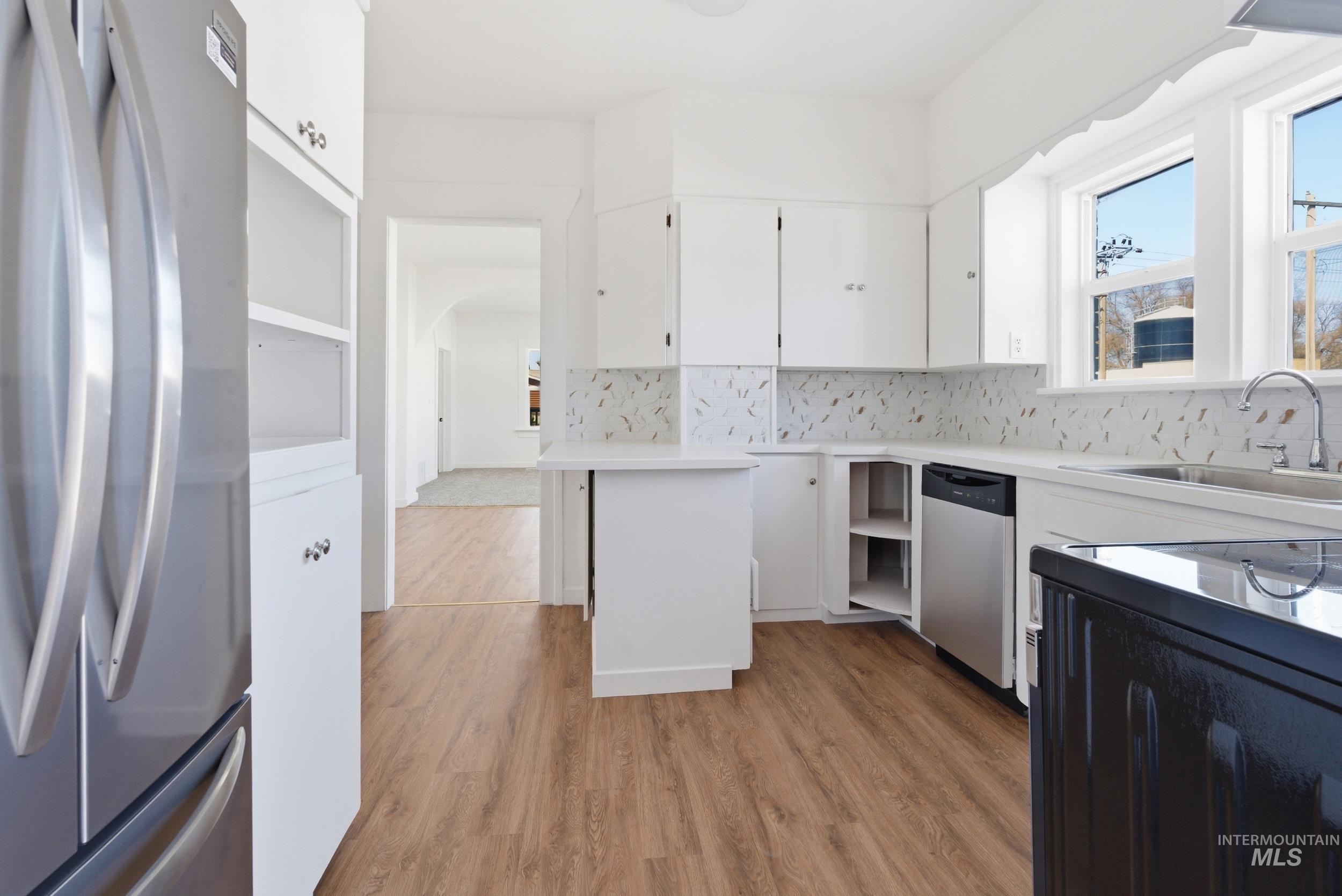 107 West Main Street Declo, ID 83323 - Photo 4 of 32 Kitchen with stainless steel appliances, white cabinetry, light wood-type flooring, light countertops, and arched walkways