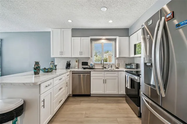 a kitchen with white cabinets stainless steel appliances a sink and a window
