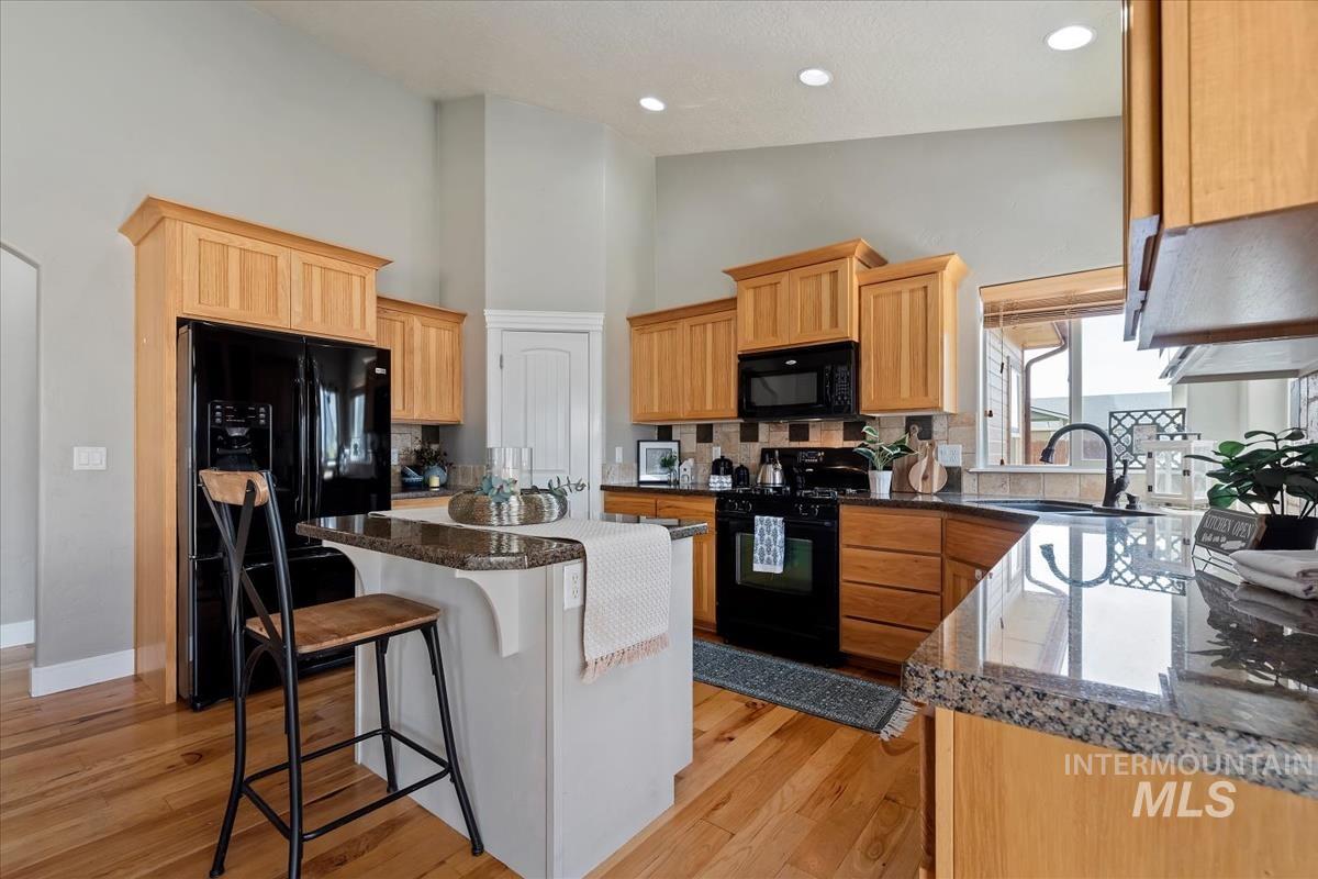 640 Southwest Miner Street Mountain Home, ID 83647 - Photo 31 of 35 Kitchen featuring wood-finish flooring, light wood cabinetry, stone countertops, and black appliances