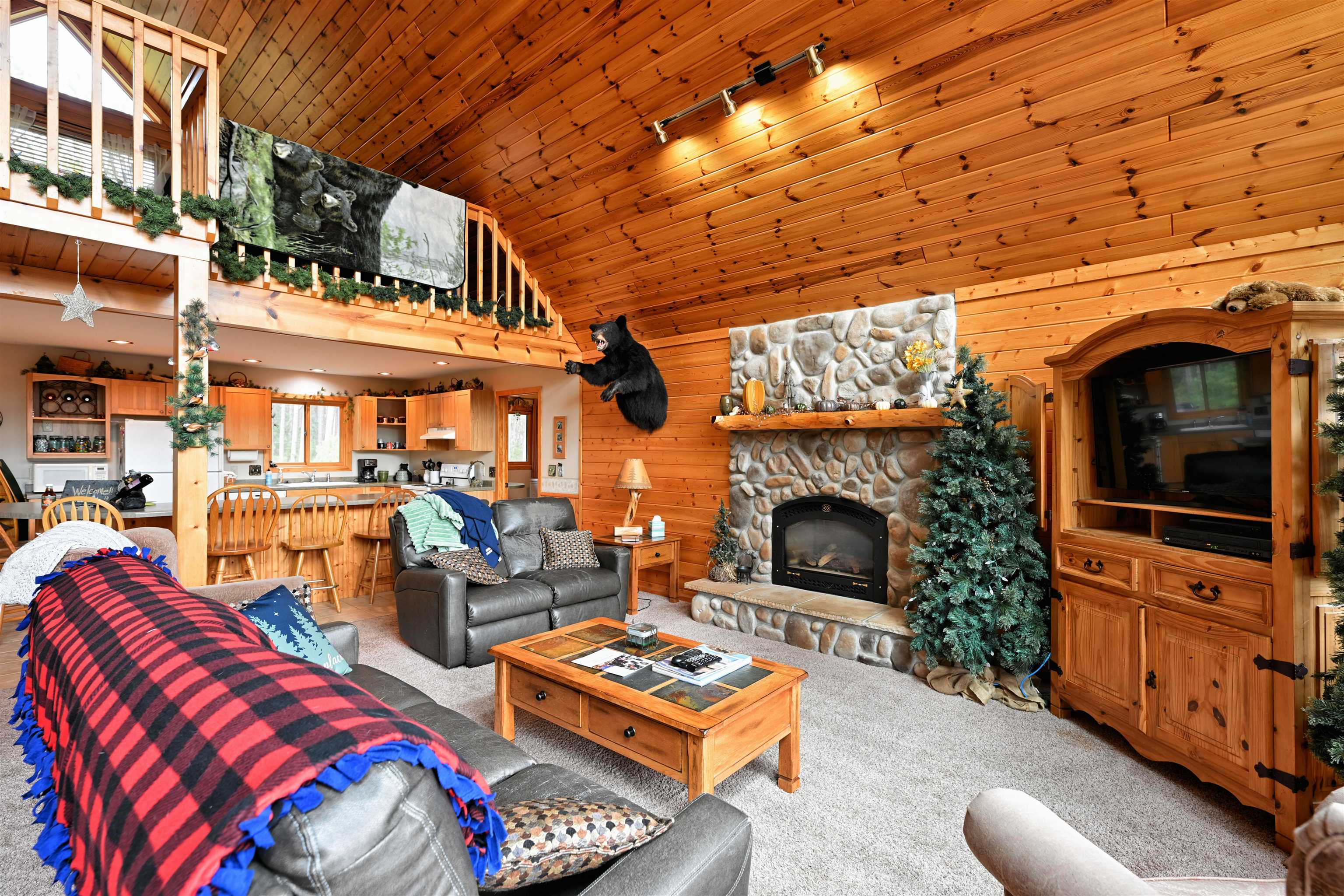 13672 East Short Road Gordon, WI 54838 - Photo 51 of 75 Living area with high vaulted ceiling, wooden walls, wooden ceiling, carpet floors, and a stone fireplace