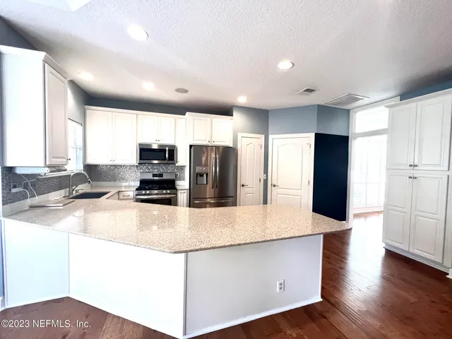 a view of a kitchen with kitchen island a large counter top space a sink stainless steel appliances and cabinets
