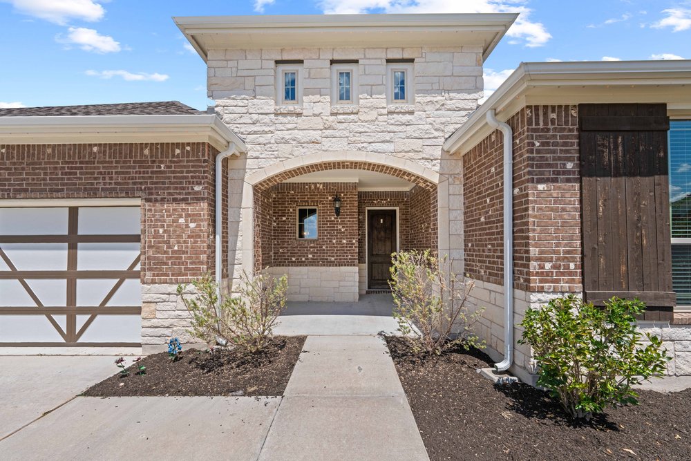 4208 Brean Down Road Pflugerville, TX 78660 - Photo 10 of 31 A concrete walkway leads to an arched stone entryway framed by classic brick masonry.