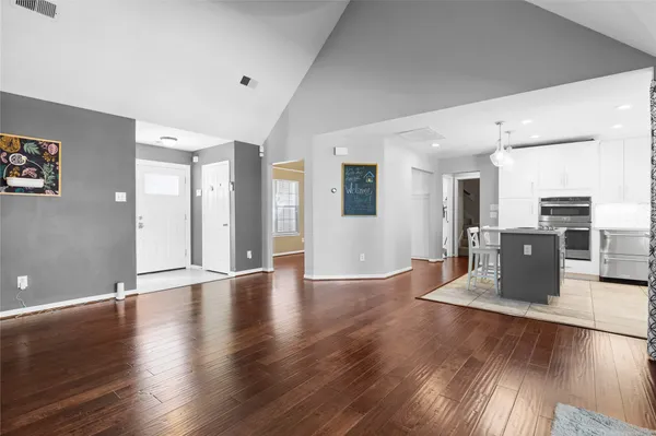 a view of an empty room with wooden floor and a kitchen