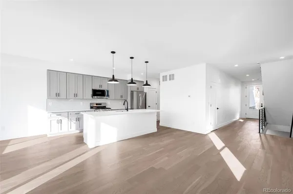 a kitchen with stainless steel appliances a stove top oven a sink a refrigerator white cabinets and wooden floor