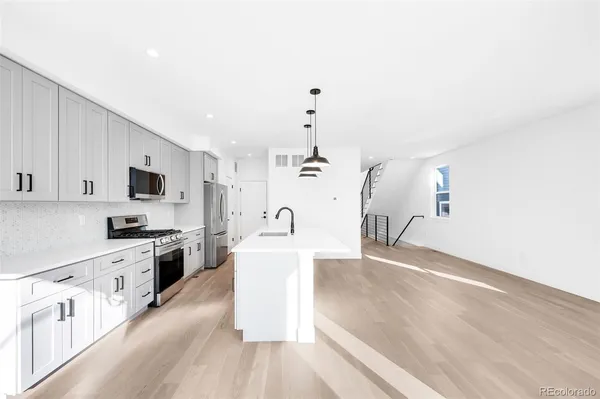 a kitchen with stainless steel appliances a refrigerator a sink dishwasher a stove and white cabinets with wooden floor