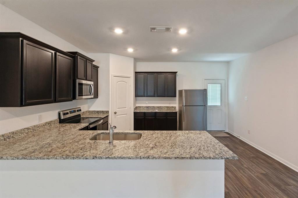 16429 Farmhouse Lane Elgin, TX 78621 - Photo 6 of 22 Kitchen featuring granite-look countertops, dark wood cabinetry, stainless steel appliances, and recessed lighting