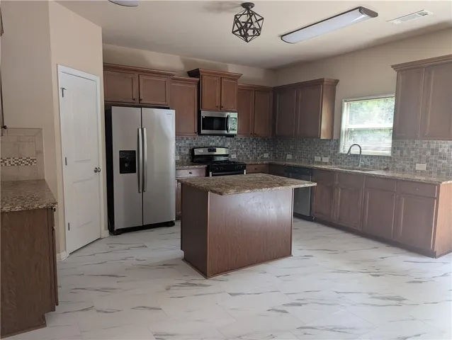 a kitchen with stainless steel appliances granite countertop a stove top oven a refrigerator and a sink