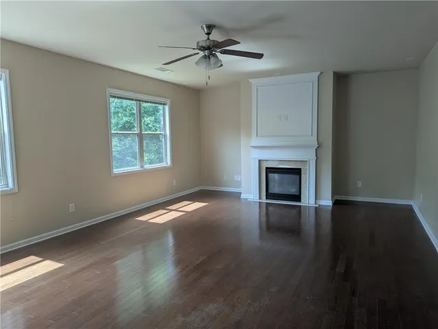 an empty room with wooden floor a chandelier fan and windows