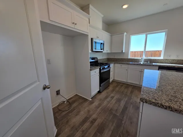 a kitchen with granite countertop a sink a stove top oven and cabinetry