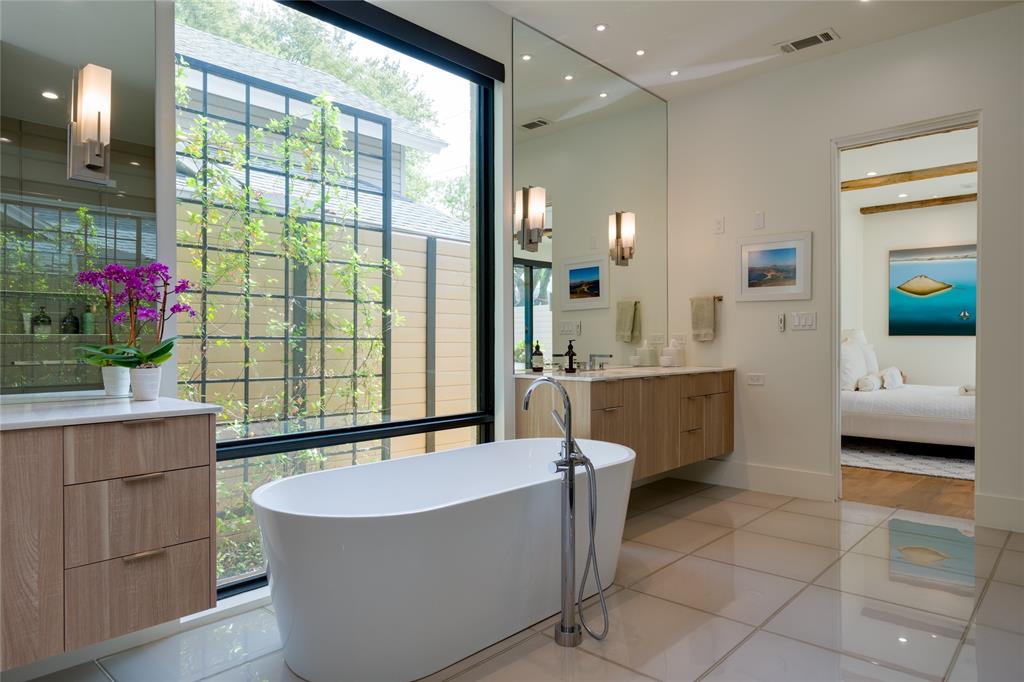 5736 Stonegate Road Dallas, TX 75209 - Photo 18 of 29 Freestanding soaking tub with floor-mounted fixture, dual wood-finish floating vanities with undermount sinks, full-height mirror, large format tile flooring, and oversized window with exterior trellis