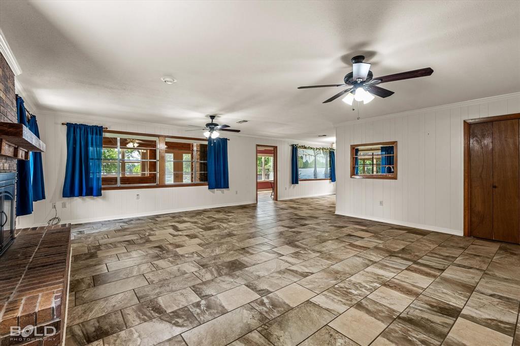 225 Marie Road Ringgold, LA 71068 - Photo 21 of 40 Spacious room featuring patterned tile flooring, a brick fireplace with wood mantel, multiple windows, white paneling, and ceiling fans