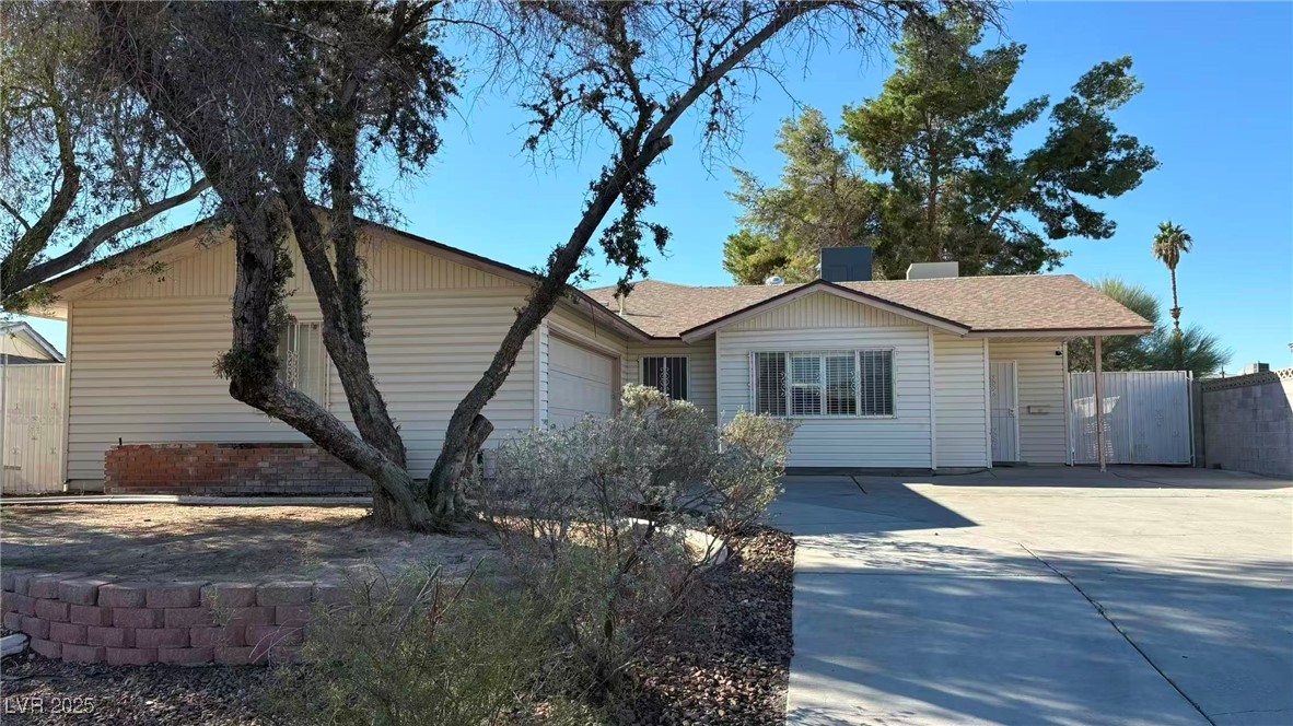 Ranch-style house with concrete driveway, a shingled roof, a garage, and a gate