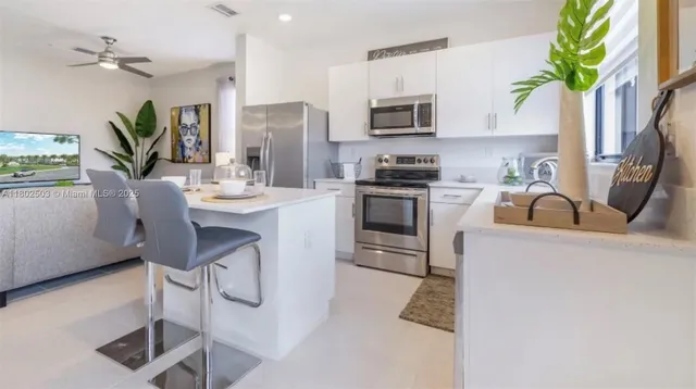 a kitchen with stainless steel appliances a stove a sink a microwave a refrigerator cabinets and a dining table