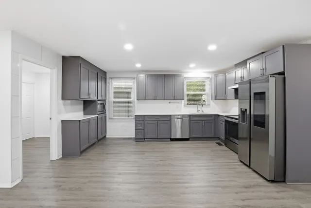 a large kitchen with a large counter top a sink stainless steel appliances and cabinets