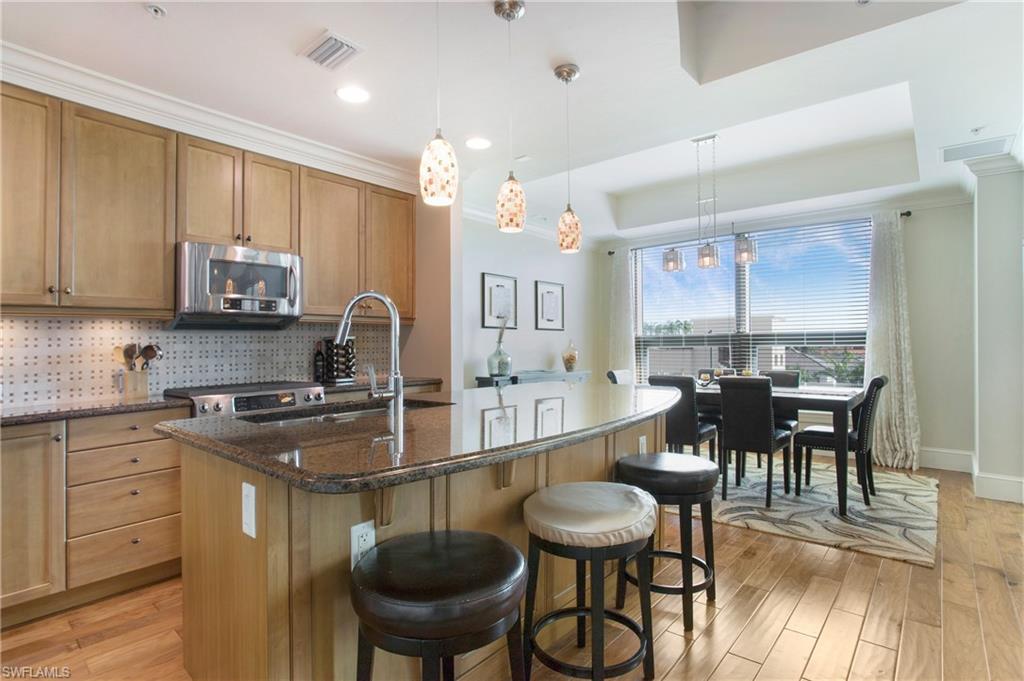 9123 Strada Place, Unit 7307 Naples, FL 34108 - Photo 14 of 49 a kitchen with stainless steel appliances granite countertop a stove top oven a sink a dining table and chairs with wooden floor