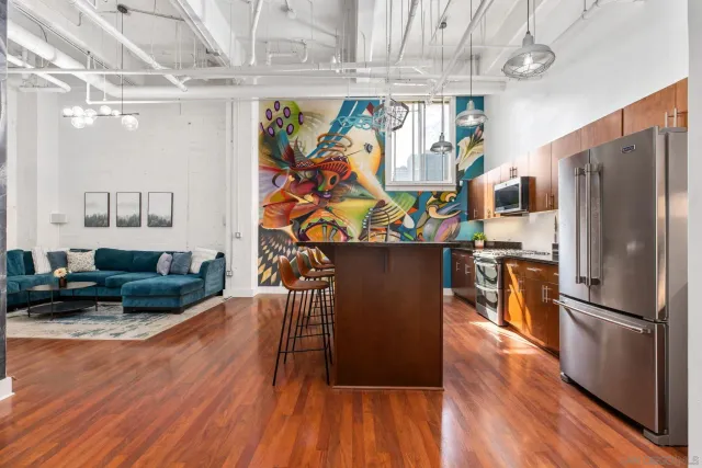 a living room with stainless steel appliances furniture wooden floor and a kitchen view