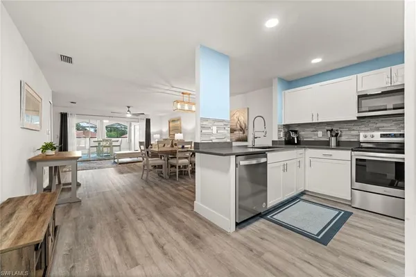 a white kitchen with wooden floors and stainless steel appliances