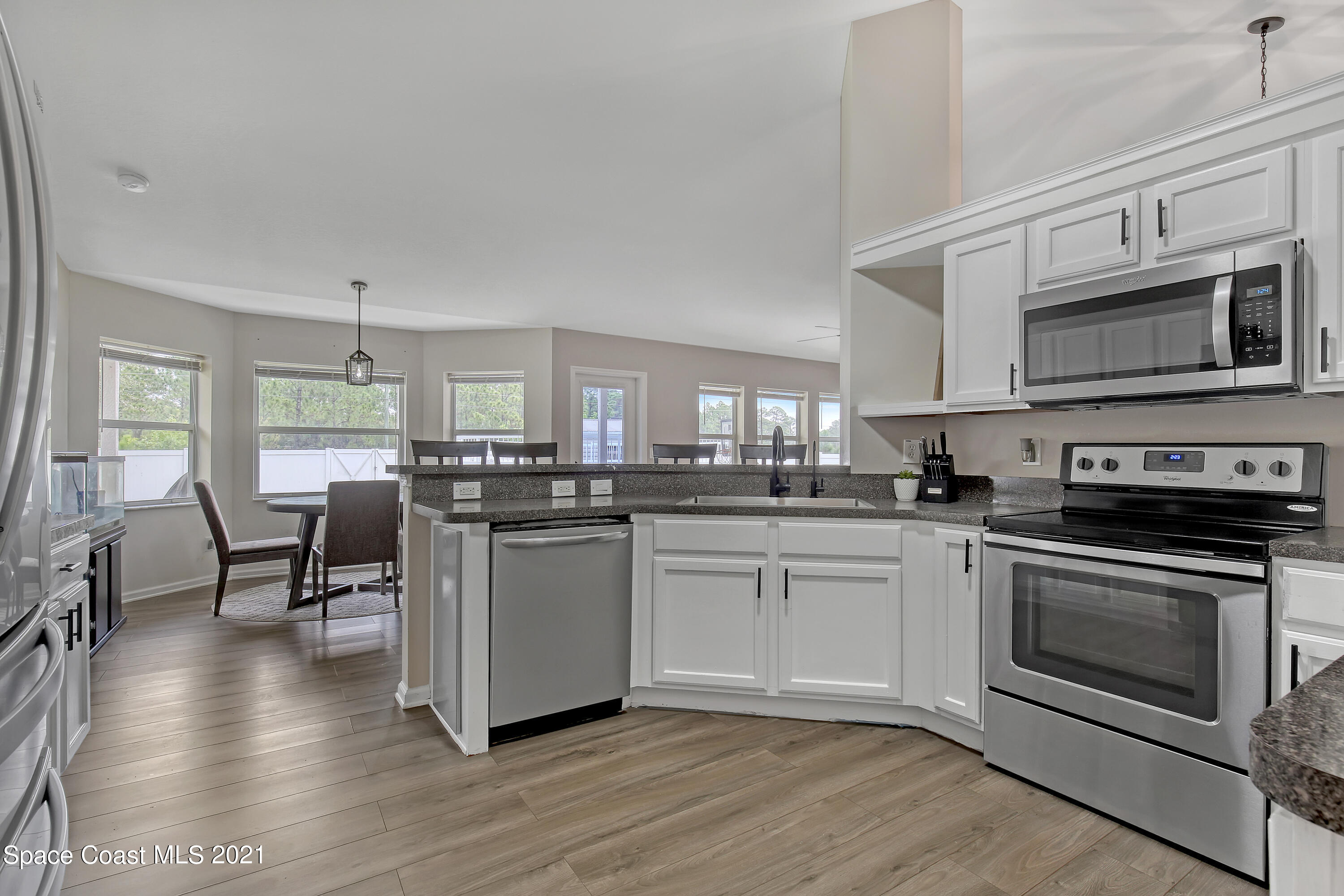 1277 Harlingen Road Southwest Palm Bay, FL 32908 - Photo 13 of 32 a kitchen with stainless steel appliances granite countertop a stove top oven a sink dishwasher a dining table and chairs with wooden floor