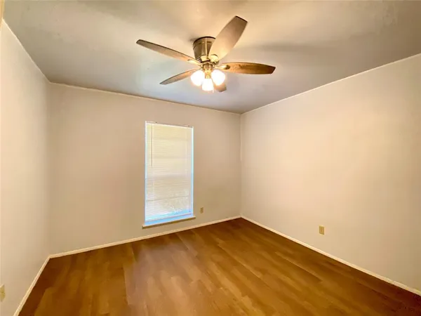a view of an empty room with wooden floor and a ceiling fan