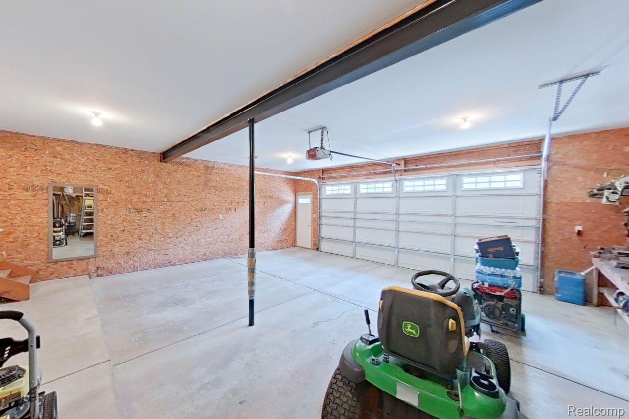10201 Washburn Road Goodrich, MI 48438 - Photo 67 of 85 Spacious garage featuring a large overhead door with transom windows, exposed OSB wall paneling, a concrete floor, and integrated ceiling lighting