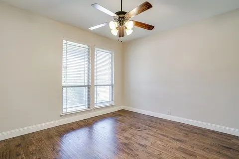 an empty room with wooden floor chandelier fan and windows