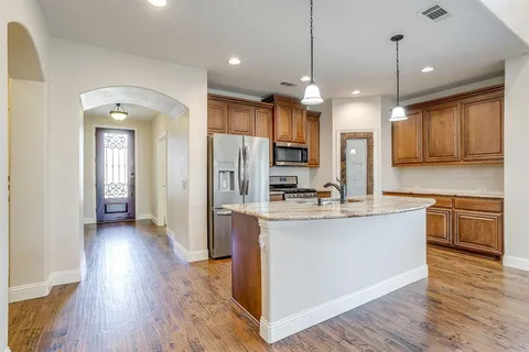a kitchen with stainless steel appliances granite countertop a refrigerator a sink dishwasher a kitchen island with wooden floor and cabinets